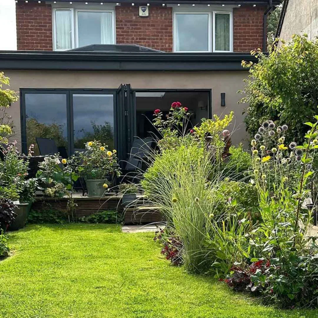 Black Korniche aluminium Bifold Doors spanning a modern living room, with sofas, wooden flooring and views of the garden.