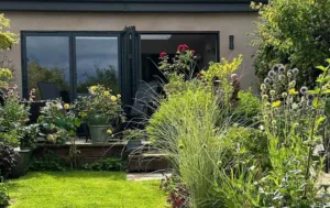 Black Korniche aluminium Bifold Doors spanning a modern living room, with sofas, wooden flooring and views of the garden.