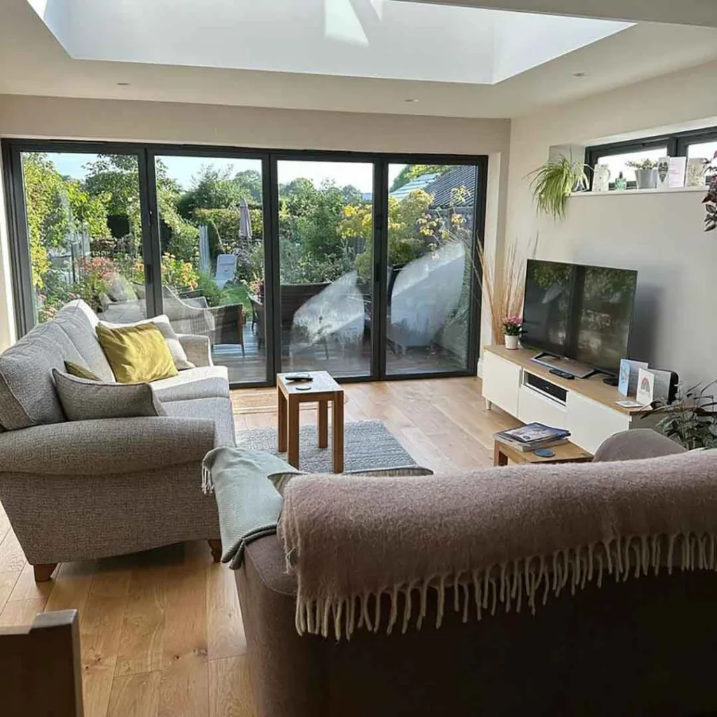 Dark grey Korniche aluminium Bifold Doors partially folded open on a rear house extension, viewed from a landscaped garden.