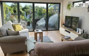 Dark grey Korniche aluminium Bifold Doors partially folded open on a rear house extension, viewed from a landscaped garden.