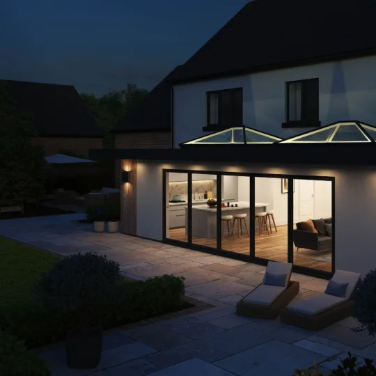 Nighttime exterior view of a home extension featuring two illuminated Korniche Roof Lanterns and Korniche bifold doors leading to a patio.