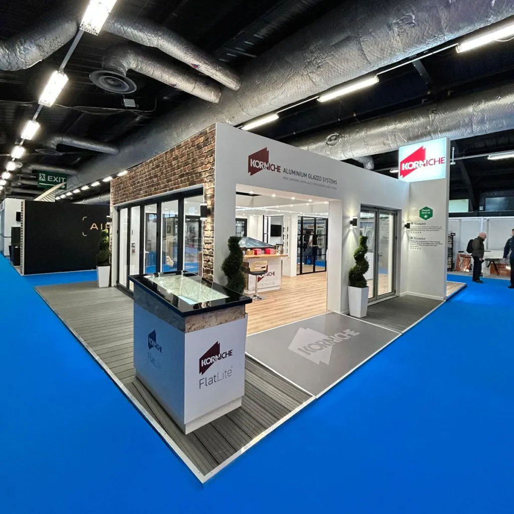 A wide view of the Korniche exhibition stand, brightly lit and showcasing the roof lantern, bi-fold door, and internal glass partition displays.