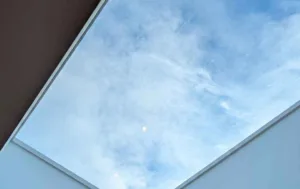 Interior view looking up through a Korniche Flat Glass Rooflight with a white internal finish, showing blue sky and clouds above.